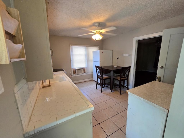 42 W 26th St, San Angelo, TX 76903 - kitchen featuring freestanding refrigerator, ceiling fan, tile counters, light tile patterned floors, and a textured ceiling