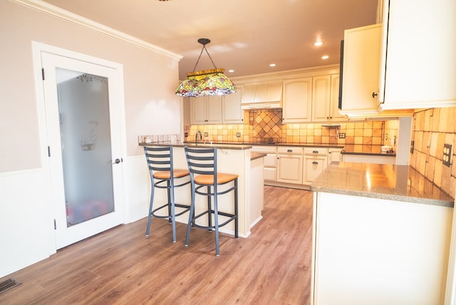 kitchen featuring dark stone counters, hanging light fixtures, kitchen peninsula, custom range hood, and light wood-type flooring