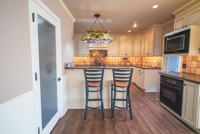 kitchen featuring black oven, a breakfast bar, built in microwave, decorative light fixtures, and cream cabinetry