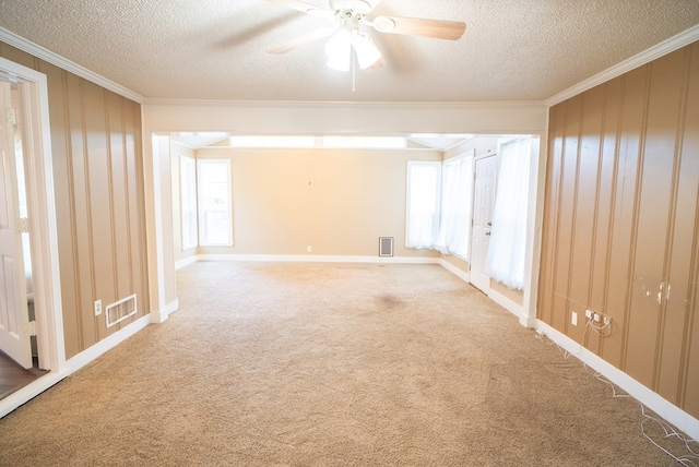 carpeted empty room with ceiling fan, ornamental molding, a textured ceiling, and wood walls