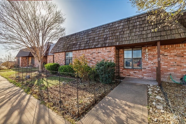 view of front facade featuring mansard roof, brick siding, and fence