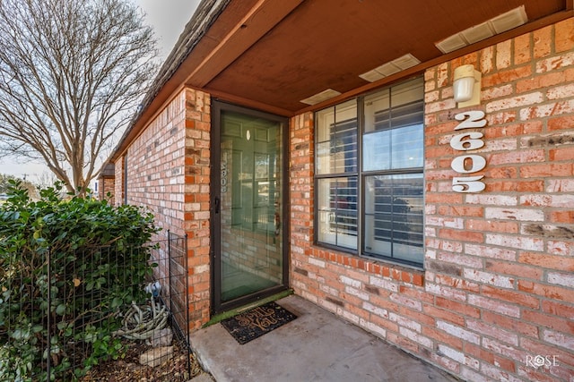 doorway to property featuring visible vents and brick siding