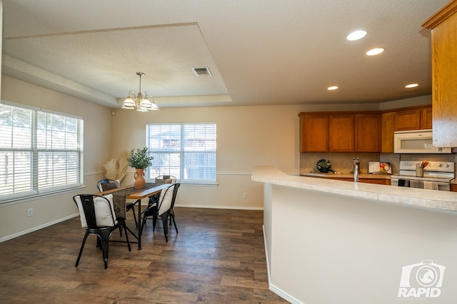 kitchen with dark hardwood / wood-style flooring, hanging light fixtures, white appliances, a tray ceiling, and an inviting chandelier