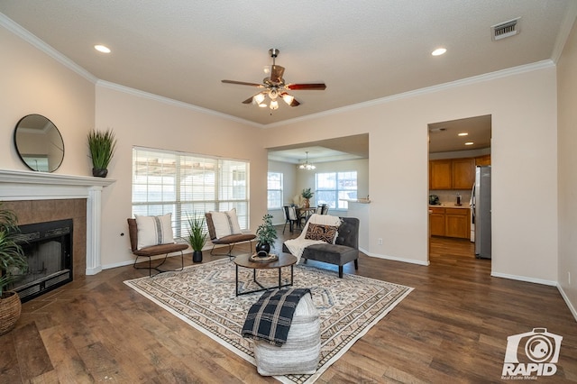 living room featuring a tiled fireplace, ornamental molding, dark wood-type flooring, and ceiling fan with notable chandelier