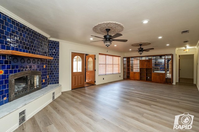 unfurnished living room with a tiled fireplace, ornamental molding, light hardwood / wood-style floors, and ceiling fan