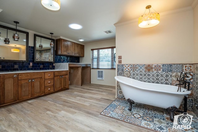 kitchen with heating unit, backsplash, hanging light fixtures, crown molding, and light hardwood / wood-style flooring