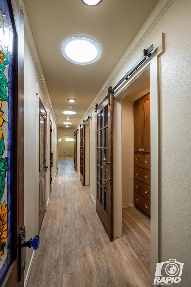 hallway featuring hardwood / wood-style flooring, ornamental molding, and a barn door