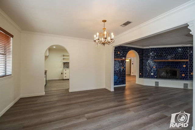 spare room featuring dark wood-type flooring, crown molding, a tiled fireplace, and a notable chandelier