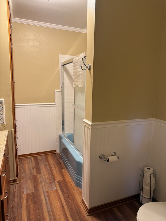 bathroom with wainscoting, wood finished floors, vanity, combined bath / shower with glass door, and toilet