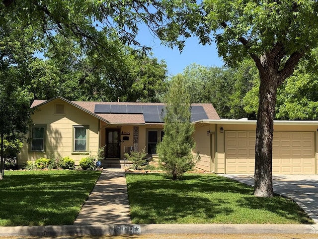 ranch-style house featuring roof mounted solar panels, an attached garage, concrete driveway, and a front yard