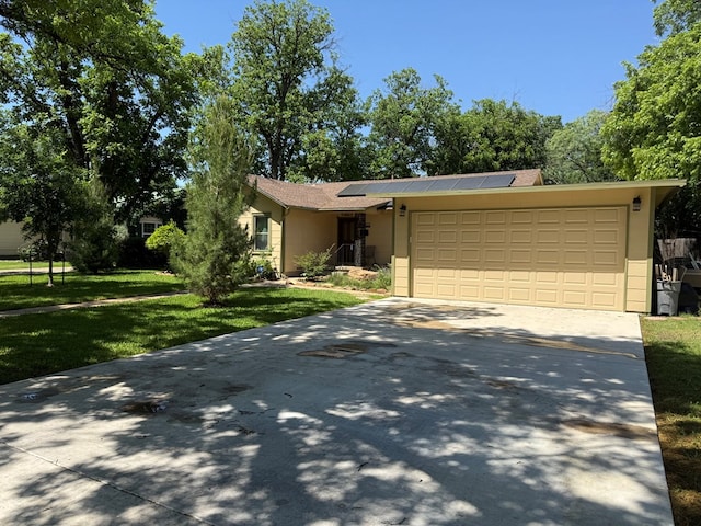 view of front facade featuring a garage, concrete driveway, solar panels, and a front yard
