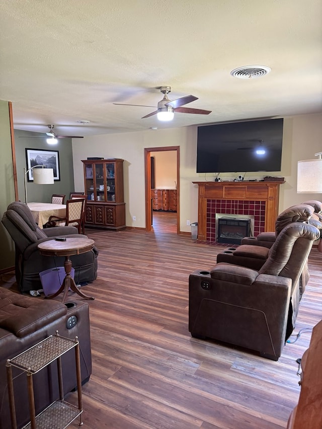 living area with ceiling fan, visible vents, a fireplace, wood finished floors, and baseboards