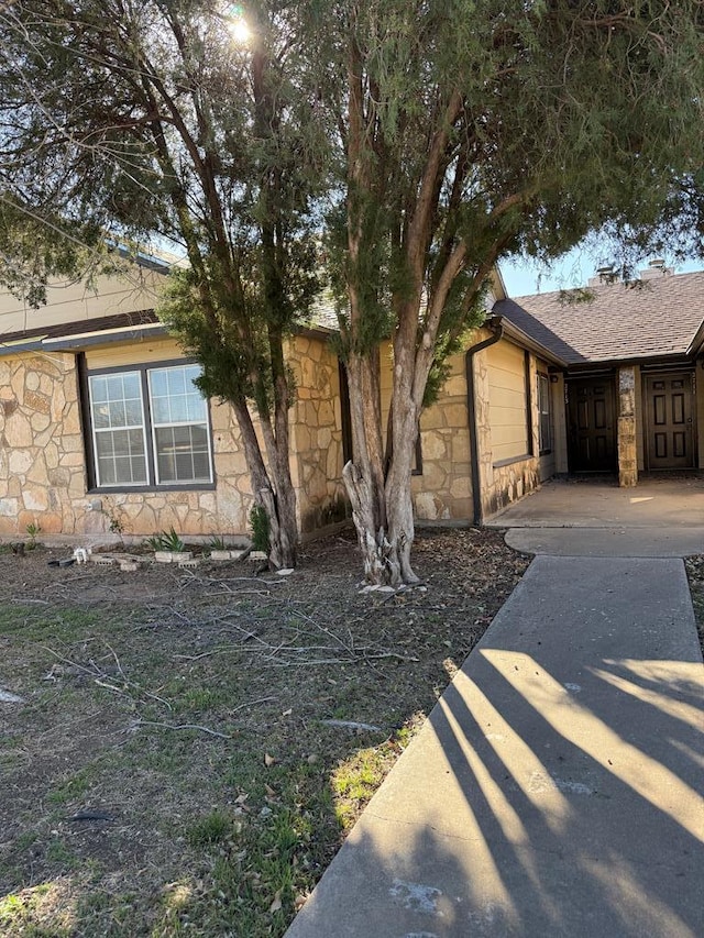 view of front of home with stone siding and roof with shingles