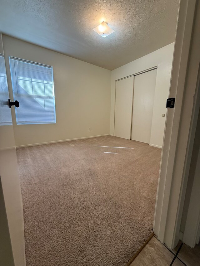 unfurnished bedroom with a closet, baseboards, light colored carpet, and a textured ceiling