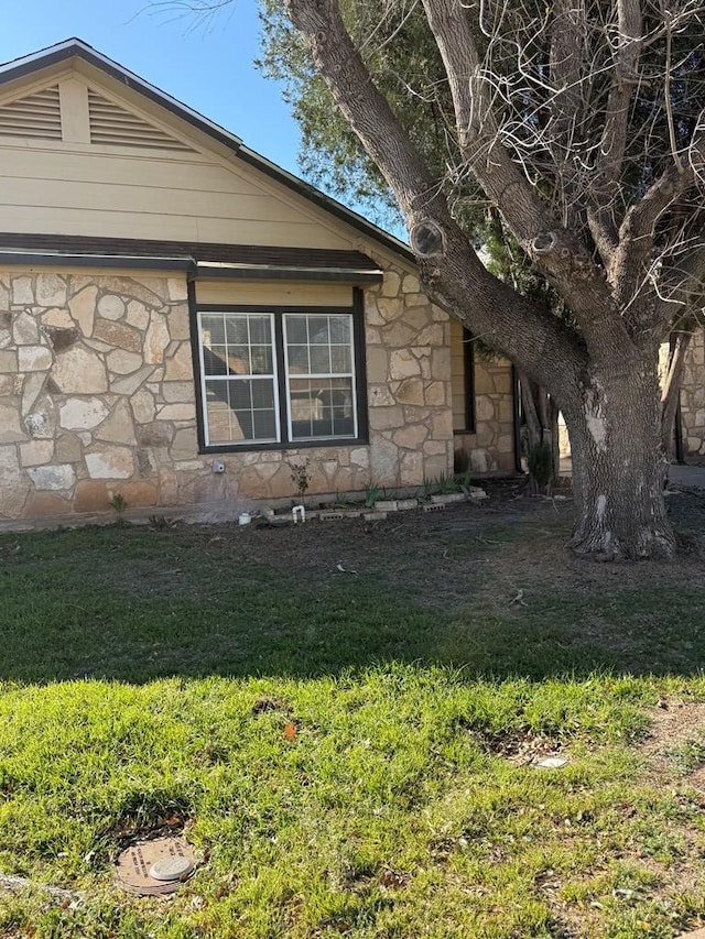 view of side of property featuring stone siding and a yard