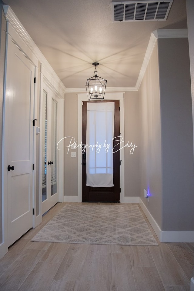 doorway with an inviting chandelier, ornamental molding, and light hardwood / wood-style floors