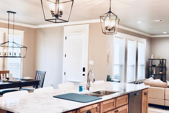 kitchen featuring pendant lighting, dishwasher, a chandelier, a kitchen island with sink, and light stone counters