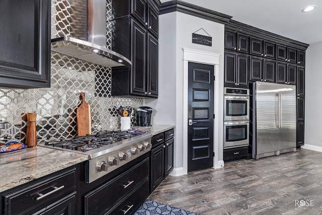 kitchen with tasteful backsplash, dark hardwood / wood-style flooring, light stone counters, stainless steel appliances, and wall chimney exhaust hood