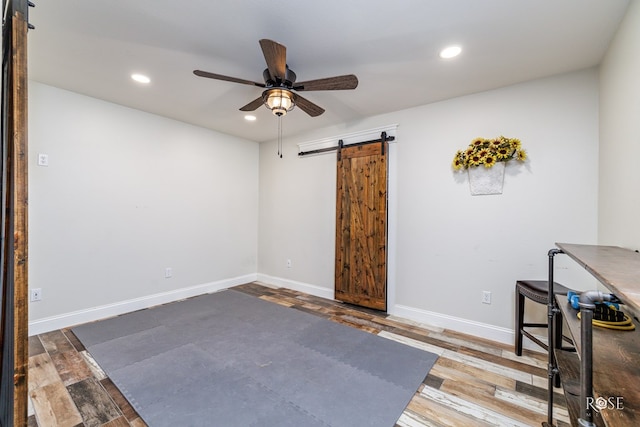 unfurnished office with wood-type flooring, a barn door, and ceiling fan