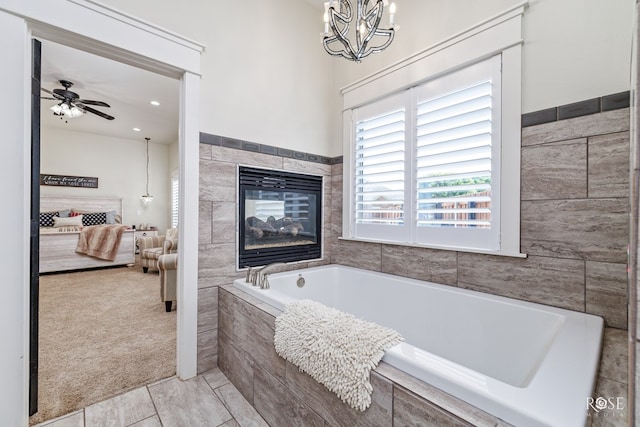 bathroom with ceiling fan with notable chandelier, tile patterned flooring, a tile fireplace, and tiled tub