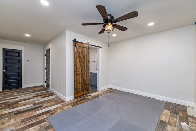 spare room featuring a barn door, dark wood-type flooring, and ceiling fan