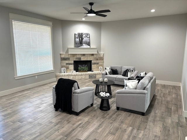 living room featuring hardwood / wood-style floors, a stone fireplace, and ceiling fan