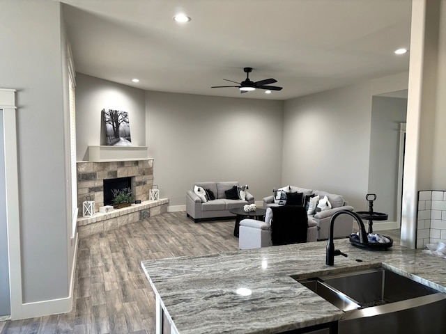 kitchen featuring a stone fireplace, sink, light stone counters, wood-type flooring, and ceiling fan