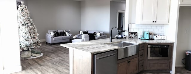 kitchen with sink, white cabinets, kitchen peninsula, stainless steel appliances, and light stone countertops