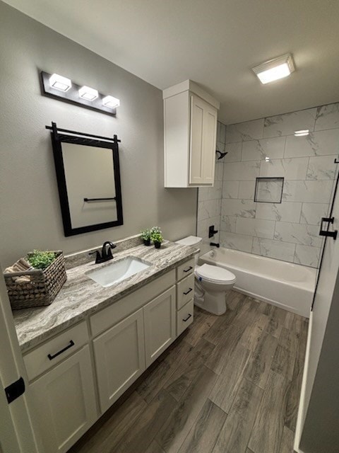 full bathroom featuring vanity, hardwood / wood-style floors, tiled shower / bath combo, and toilet