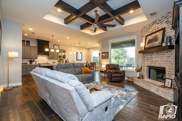 living room with beamed ceiling, a brick fireplace, coffered ceiling, and ceiling fan