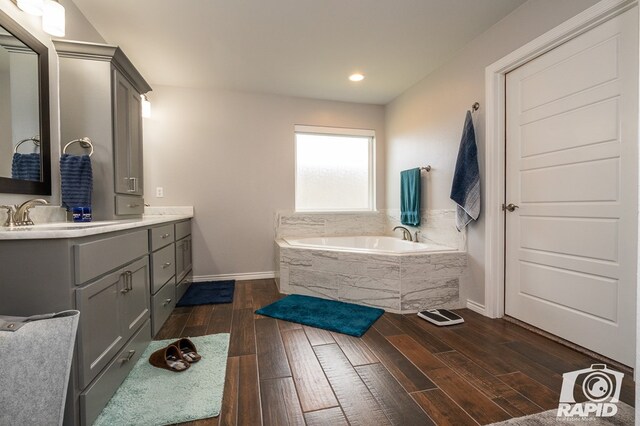 bathroom featuring hardwood / wood-style flooring, vanity, and a relaxing tiled tub