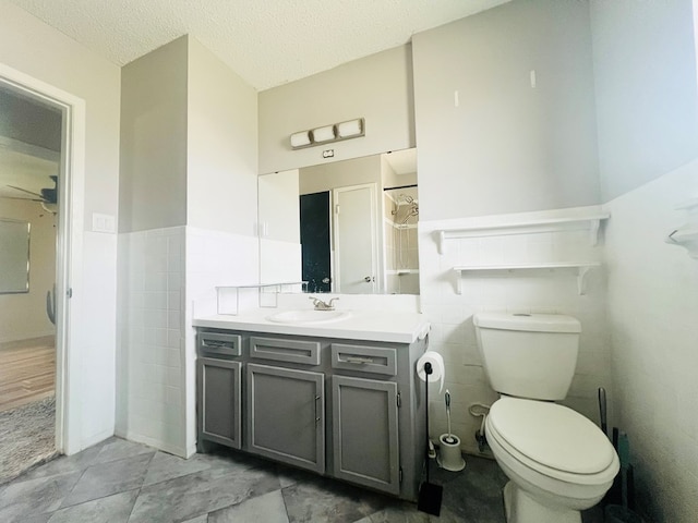 bathroom with vanity, toilet, a textured ceiling, and tile walls