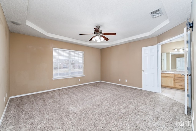 unfurnished bedroom with light carpet, ensuite bath, a raised ceiling, and a textured ceiling