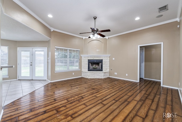 unfurnished living room featuring french doors, crown molding, dark hardwood / wood-style flooring, ceiling fan, and a fireplace