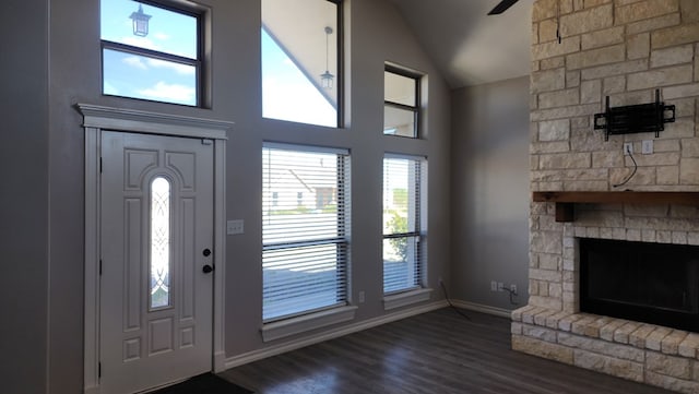 foyer entrance with a stone fireplace, dark wood-type flooring, and high vaulted ceiling