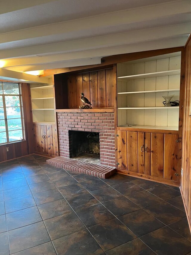 unfurnished living room featuring a brick fireplace, beam ceiling, built in shelves, and wood walls