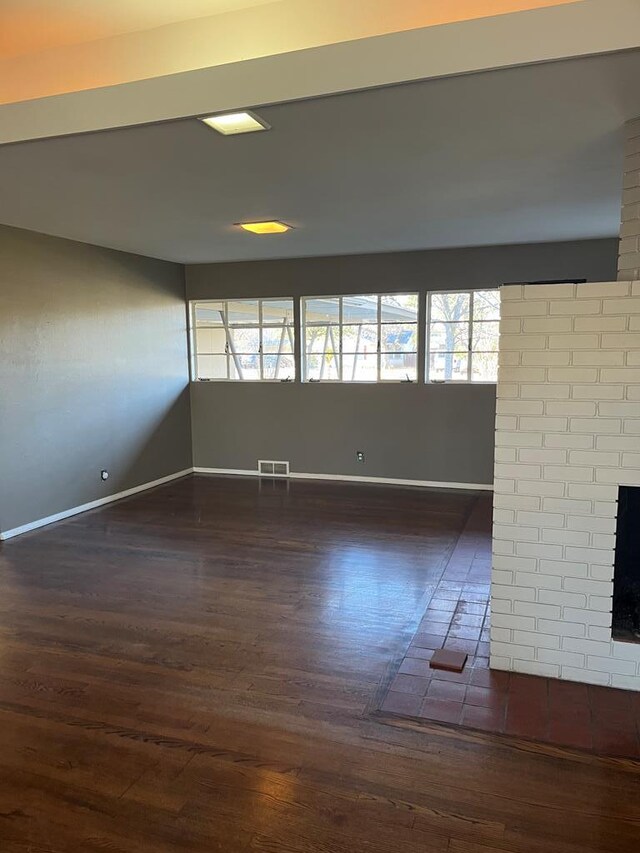 spare room with a brick fireplace and dark hardwood / wood-style floors