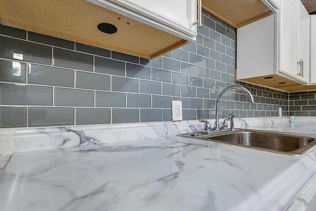 room details featuring light stone counters, sink, decorative backsplash, and white cabinets