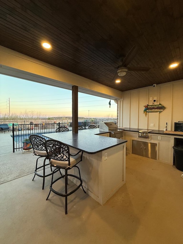 patio terrace at dusk featuring exterior kitchen, outdoor wet bar, a grill, and ceiling fan