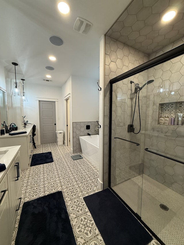 bathroom with a stall shower, a soaking tub, two vanities, and visible vents