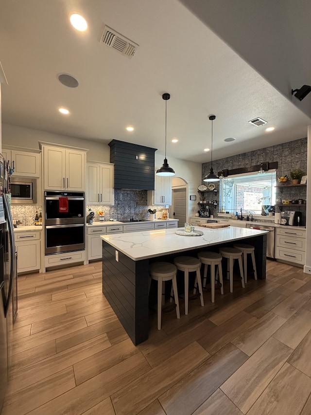 kitchen with light wood-style floors, visible vents, stainless steel appliances, and backsplash