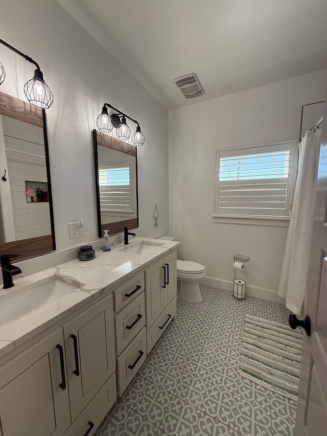 full bathroom featuring toilet, double vanity, a sink, and visible vents