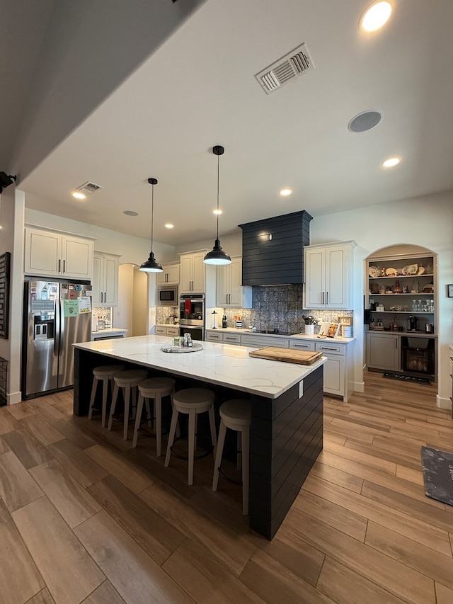 kitchen with stainless steel appliances, a spacious island, wood finished floors, visible vents, and backsplash