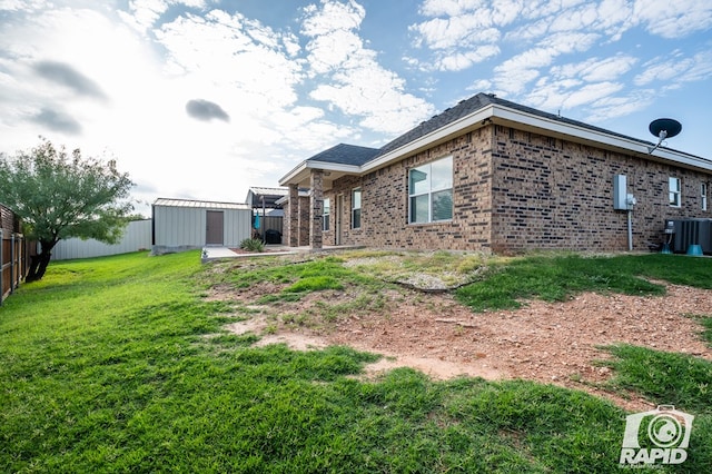 rear view of property with a storage shed, a yard, and central AC