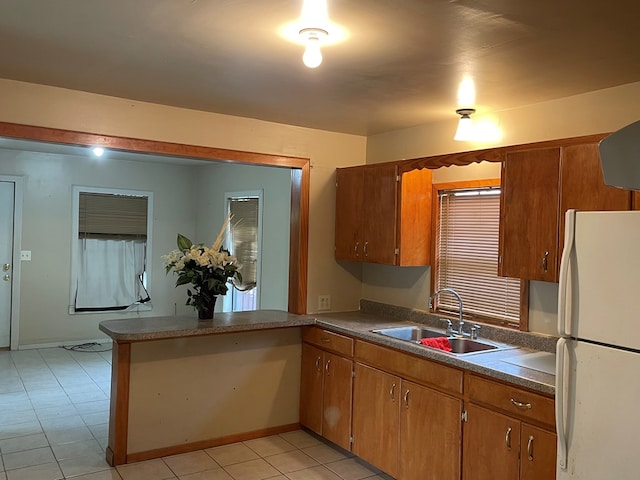 kitchen featuring a sink, light tile patterned floors, freestanding refrigerator, and brown cabinets