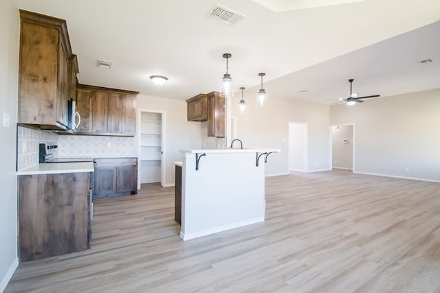 kitchen with sink, ceiling fan, hanging light fixtures, a kitchen bar, and light wood-type flooring