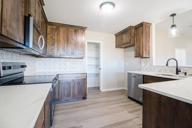 kitchen with appliances with stainless steel finishes, pendant lighting, sink, light stone counters, and light wood-type flooring