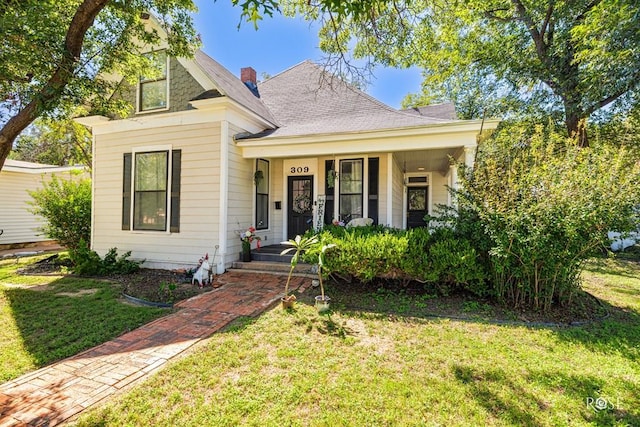 view of front of home featuring a shingled roof, a front yard, covered porch, and a chimney