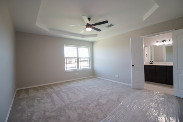 unfurnished bedroom featuring a tray ceiling, light colored carpet, ceiling fan, and ensuite bathroom