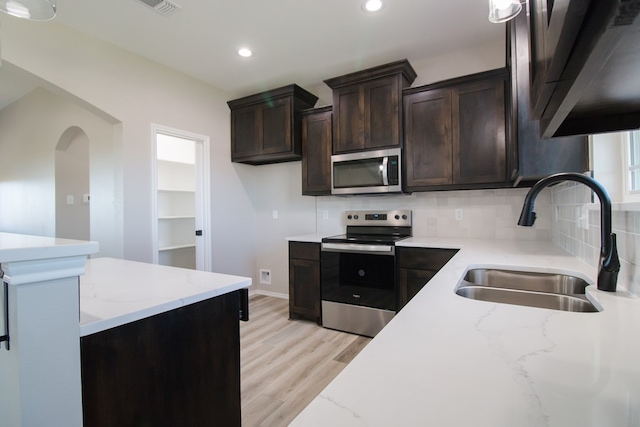 kitchen with sink, light stone counters, appliances with stainless steel finishes, light hardwood / wood-style floors, and backsplash